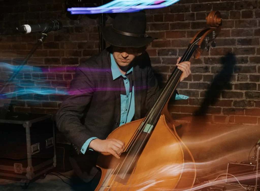 Double bass player in a hat, lit by streaks of coloured light