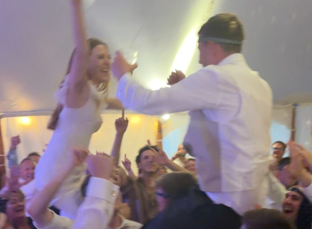 Bride and groom lifted up by a cheering crowd in a marquee