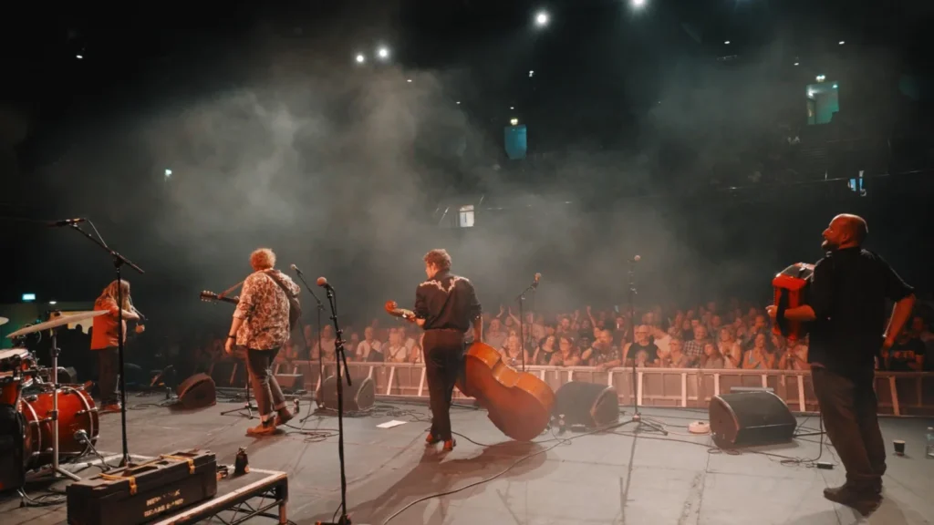 The band on stage looking out at a full arena crowd