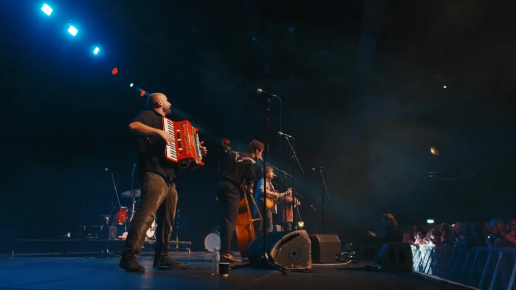 Accordion player on a blue-lit stage beside the band