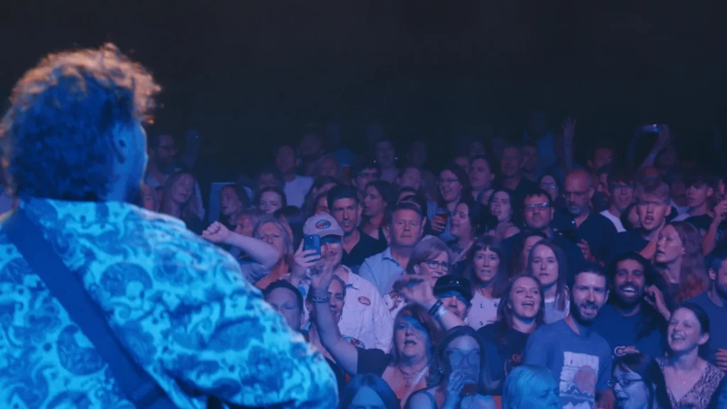 Singer with guitar raising a fist under blue stage lights
