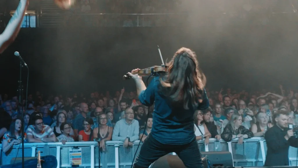 Fiddle player seen from behind, playing to a cheering crowd at the barrier
