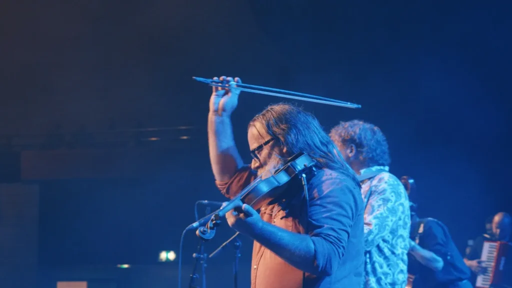 Fiddle player raising his bow under blue stage lights