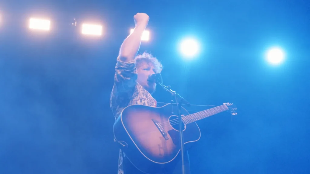 Singer with guitar raising a fist under bright blue lights