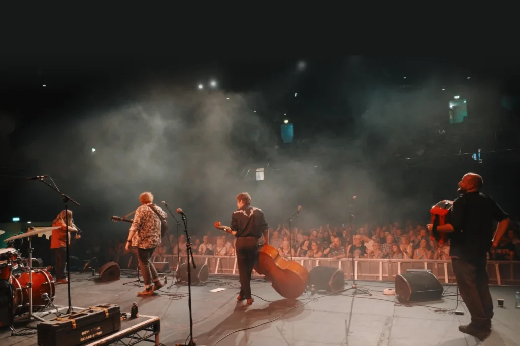 The band on stage at York Barbican, seen from behind, facing a cheering crowd